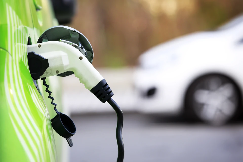Voiture électrique blanche en cours de recharge sur une borne publique dans un environnement urbain arboré