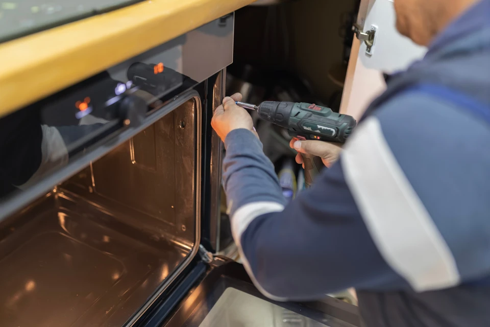 Gros plan sur un tableau électrique résidentiel moderne ouvert, montrant des disjoncteurs, des rails DIN, des câbles électriques bien organisés et étiquetés. En arrière-plan légèrement flou, aperçu d'une cuisine moderne avec électroménagers. L'image doit mettre l'accent sur la qualité, l'ordre et la précision technique de l'installation, sans personne visible.